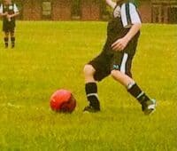 Young soccer player kicking a red ball during a match on a lush green field, showcasing youth sports and athletic activity.